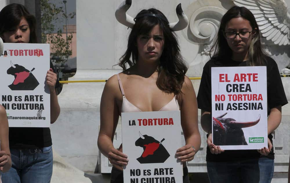 An animal rights activist, wearing a headband with bull shaped horns and partially clothed, holds a protest sign that reads in Spanish; 