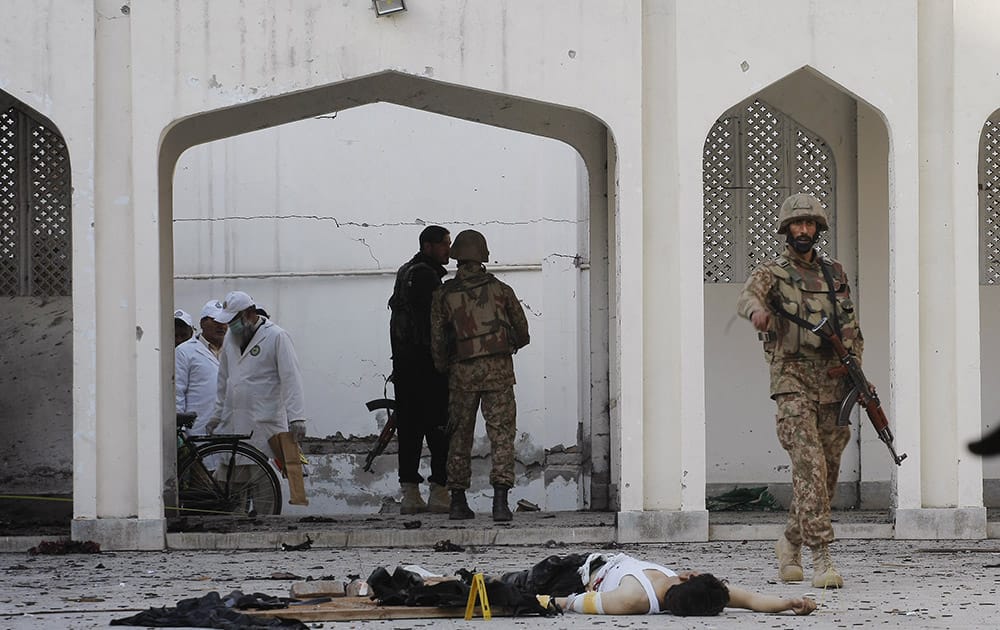 A Pakistani soldier walks past a body of a suicide attacker killed by security forces during an attack involving suicide bombers and gunmen on a Shiite mosque in Peshawar, Pakistan.