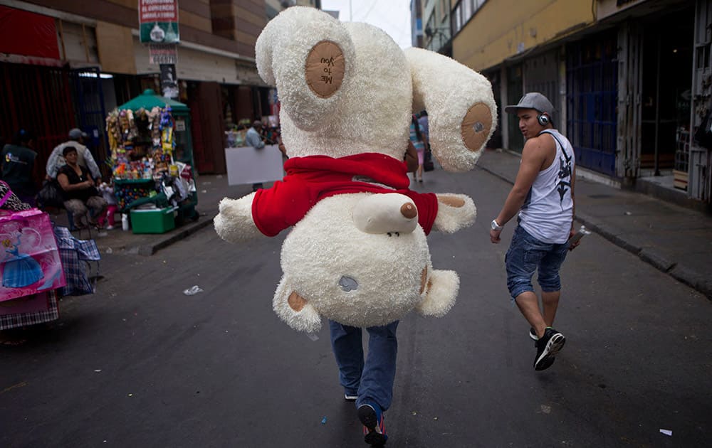 A vendor carries an oversized teddy bear to be sold as a Valentine's Day gift, in the central market of Lima, Peru.