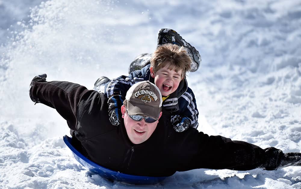 Charlie Perkins gets a ride on a snow disc from his father, David, as they speed down a snow-covered street, in Roanoke, Va. 