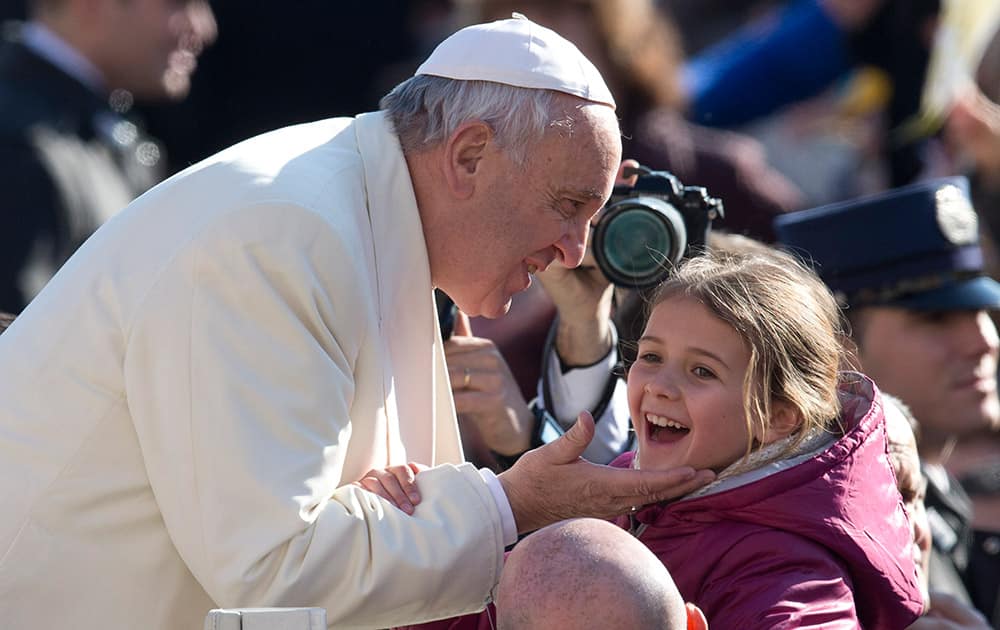 Pope Francis caresses a young girl as he arrives for his weekly general audience, in St. Peter's Square, at the Vatican.