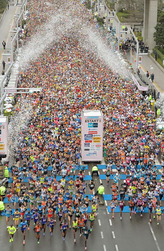 Confetti rains over runners on a street at the start of the Tokyo Marathon.