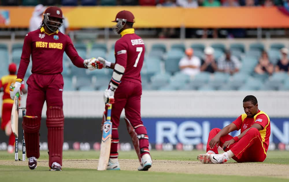 Zimbabwe's Tinashe Panyangara sits on the ground after falling while bowling as West Indies batsmen Chris Gayle and Marlon Samuels talk during their Cricket World Cup Pool B match in Canberra, Australia.