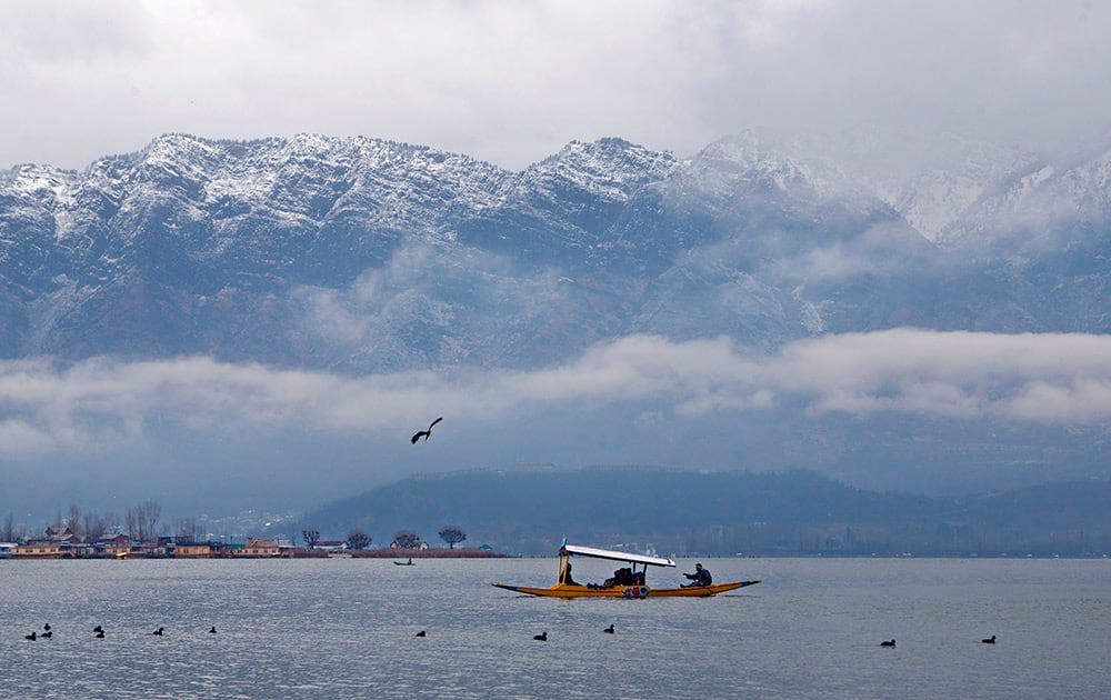 Tourists enjoy Shikara, a traditional wooden boat, with the backdrop of snow covered mountains at the Dal Lake in Srinagar.