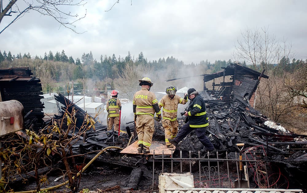 Firefighters from Lewis County Fire District No. 15 stand amongst debris from a house fire in Winlock, Wash.