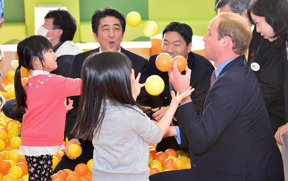 Britain’s Prince William, right, juggles balls in front of Japanese Prime Minister Shinzo Abe, left, and children at Smile Kids Park playground in Motomiya city, Japan’s northeastern prefecture of Fukushima.