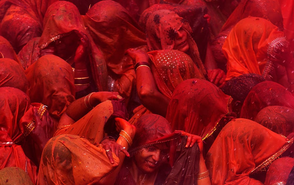 Hindu women devotees stand drenched in colored water as they participate in 