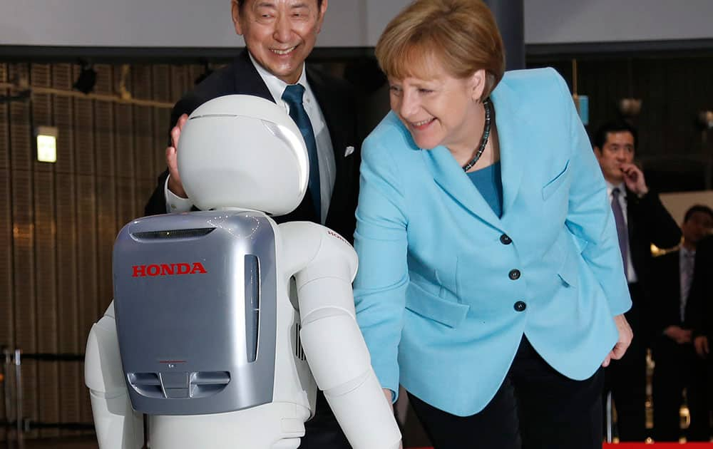 German Chancellor Angela Merkel, right, closes to shake hands with Honda Motor Co.’s interactive robot Asimo, along with the National Museum of Emerging Science and Innovation Miraikan Chief Executive Director Mamoru Mori during her visit to the the museum in Tokyo.