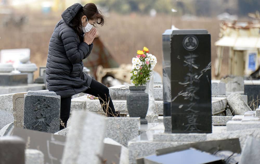 A woman prays in front of her ancestors' tomb which was damaged by the March 11, 2011 earthquake and tsunami, in Namie, Fukushima prefecture, northern Japan.