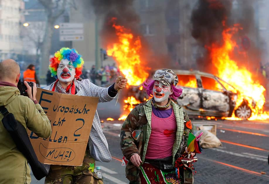 Demonstrators dressed as clowns pass by a burning police car, in Frankfurt, Germany.