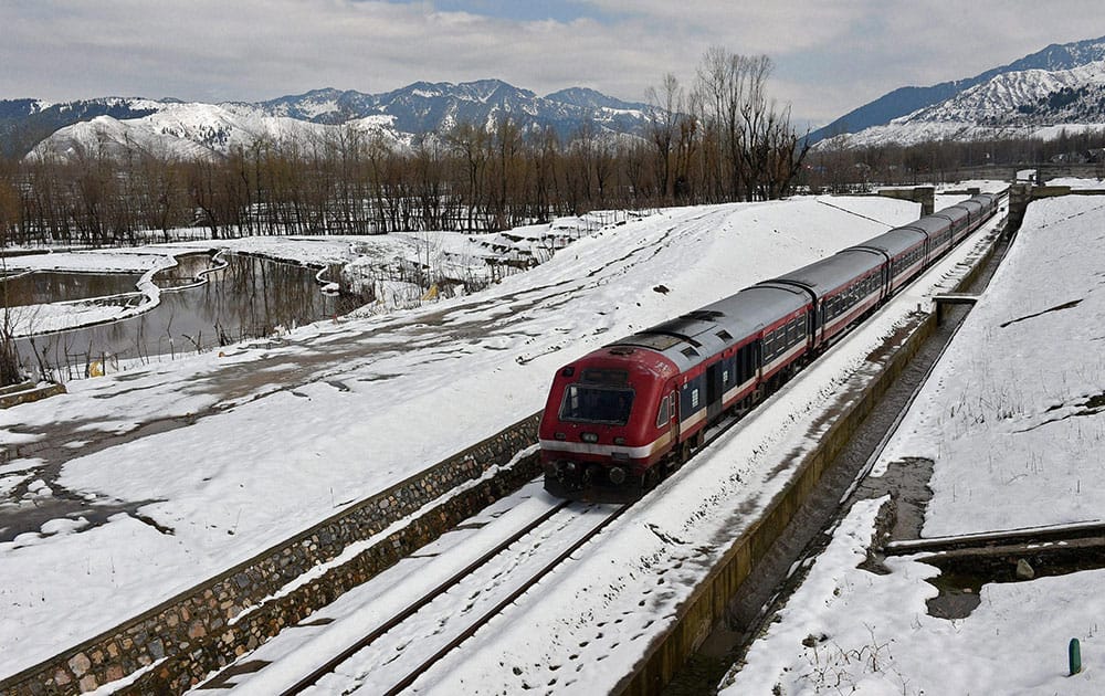 A train moves on its tracks through the snow covered field along with Jammu-Srinagar National Highway after heavy snowfall at Qazigund in Anantnag district.