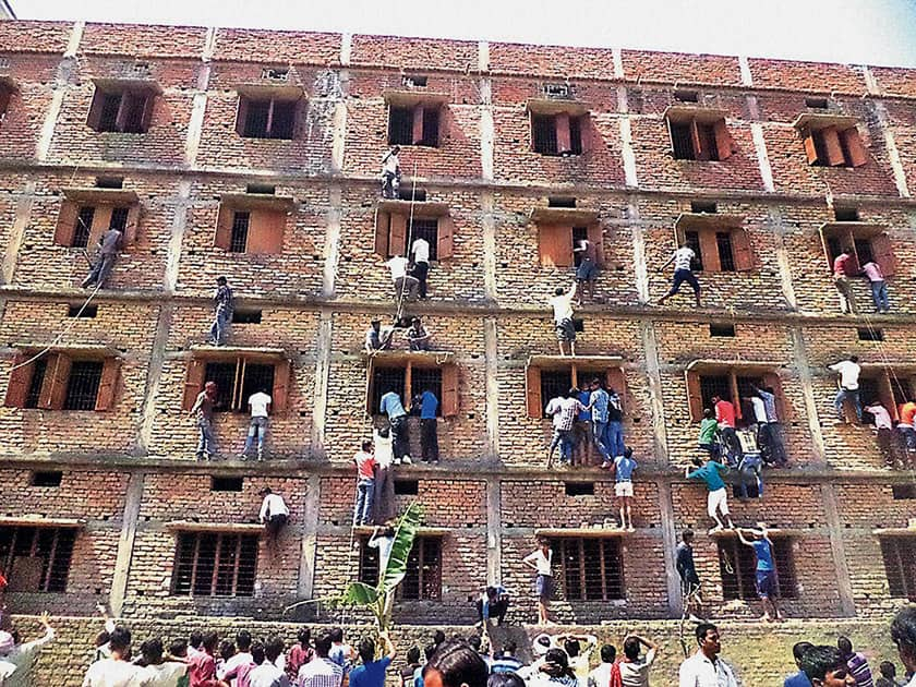 Youths climbing the building of an examination centre to help the candidates in cheating, by passing notes through the windows, during a Matriculation examination in Hajipur.