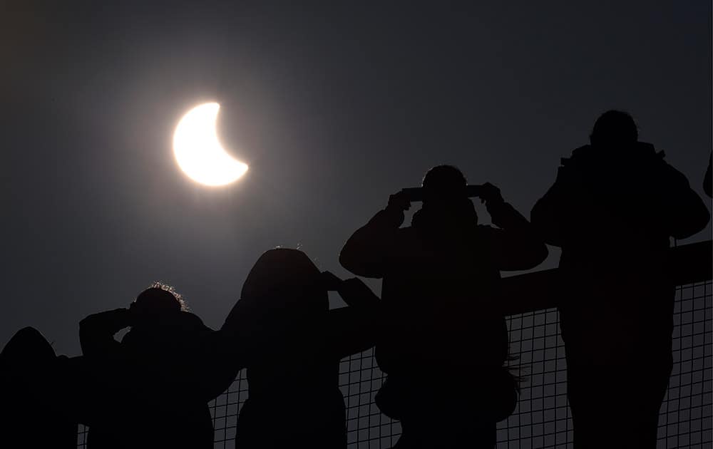 People watch as a solar eclipse begins over the Eden Project near St Austell in Cornwall, England. An eclipse is darkening parts of Europe on Friday in a rare solar event that won't be repeated for more than a decade.