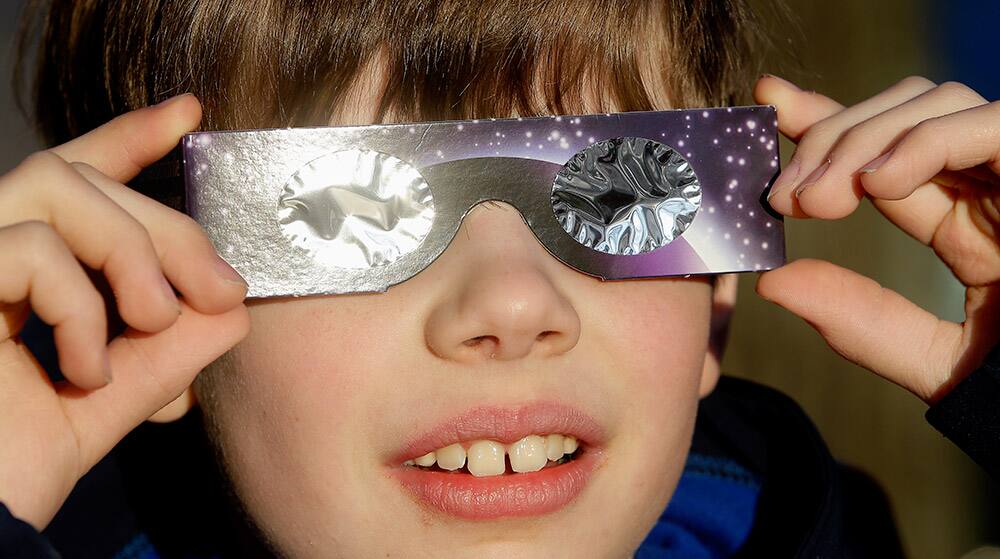 A little boy poses for a photograph and looks up to the sun wearing protective goggles in Berlin.