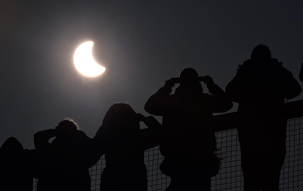 People watch as a solar eclipse begins over the Eden Project near St Austell in Cornwall, England.