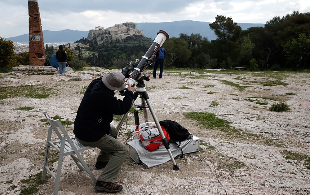 A man sets up a telescope to watch a partial eclipse of the sun as at the background is seen the ancient Acropolis hill , in Athens.