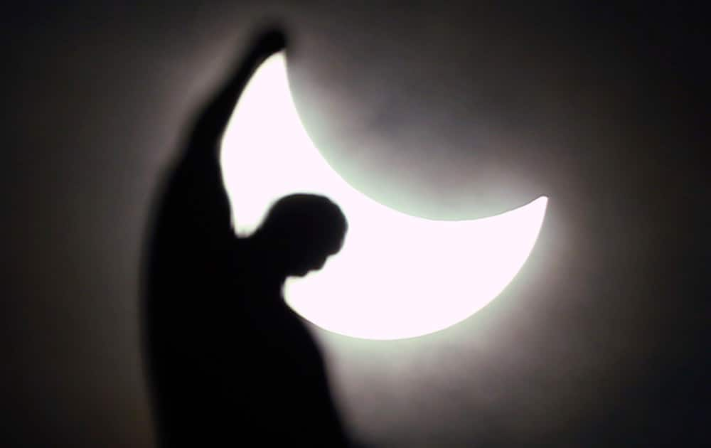 The moon starts to block the sun during a solar eclipse over a statue of the Duomo gothic cathedral in Milan, Italy.