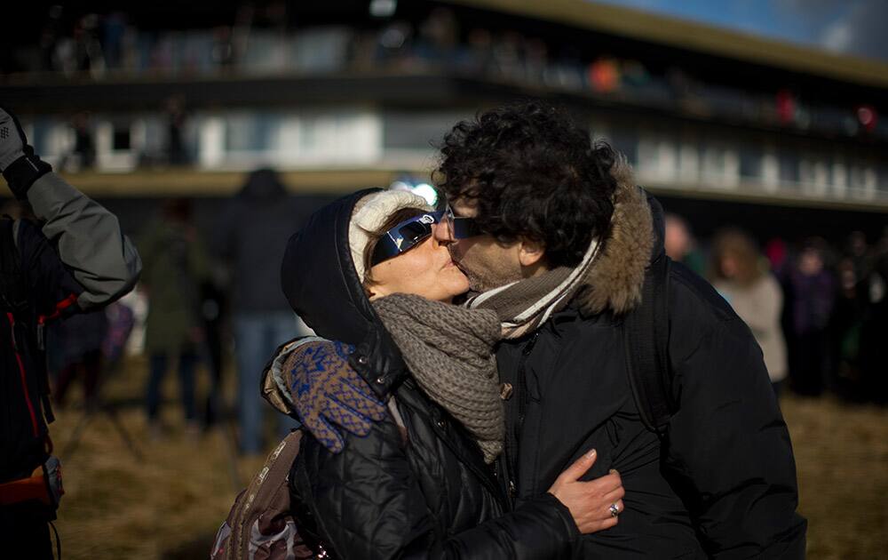 A couple kiss wearing solar protection glasses during the partial phase of a solar eclipse after totality as seen from a hill beside a hotel on the edge of the city overlooking Torshavn, the capital of the Faeroe Islands.