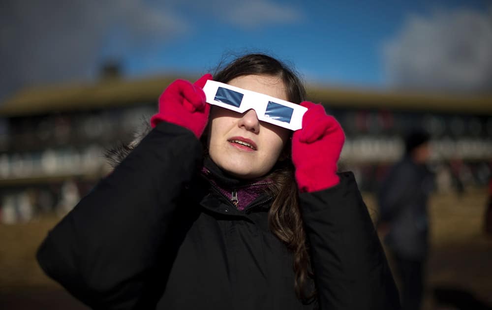 A visitor from Greece watches wearing solar protection glasses during the partial phase of a solar eclipse after totality as seen from a hill beside a hotel on the edge of the city overlooking Torshavn, the capital of the Faeroe Islands.