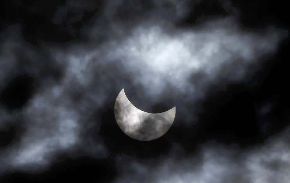 The moon starts to block the sun during a solar eclipse seen through clouds, in Skopje, Macedonia.