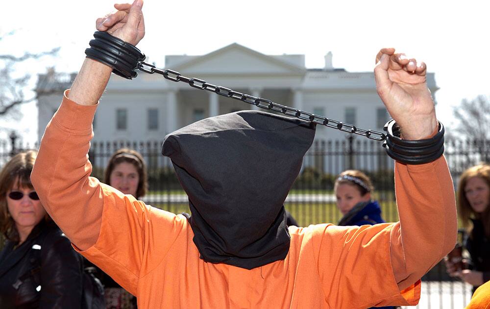 A hooded protester in an orange jumpsuit holds chained wrists high outside the White House on Pennsylvania Avenue, in front of the White House, in Washington, during a protest organized by the ANSWER Coalition protest what they say is the 