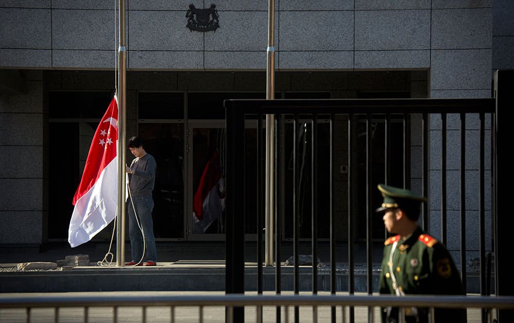 A Chinese embassy guard watches a worker prepare to raise Singaporean national flag to half-staff at the Singaporean Embassy in Beijing, Monday, March 23, 2015. 