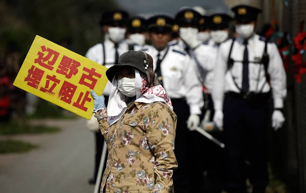 Japanese police officers stand guard as a protester against the relocation of U.S. Marine Corps Air Station Futenma, as protesters stage a rally outside Camp Schwab, an American base near a planned relocation site, in Nago, Okinawa Prefecture.