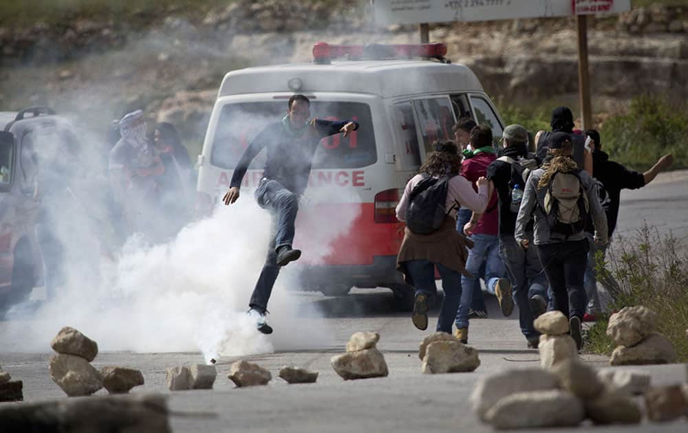 A Palestinian demonstrator kicks a tear gas canister towards Israeli soldiers as activists run away from the gas during a protest marking Land Day, in the West Bank village of Nabi Saleh near Ramallah.