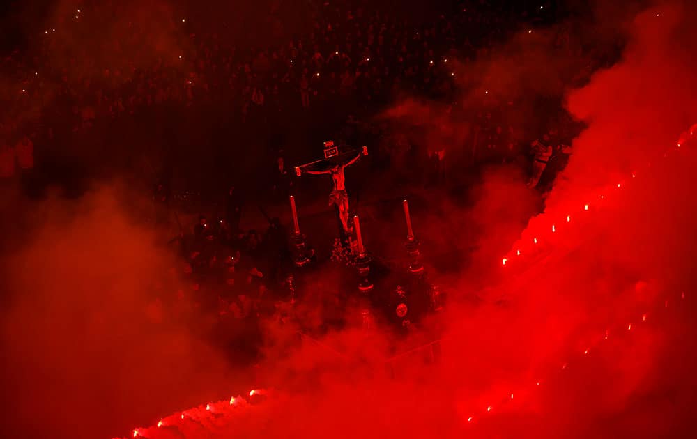 Red flares burn while penitents of the Cristo de Viga brotherhood carrying a float with a cross take part in a Holy Week procession in Jerez de la Frontera, Spain.