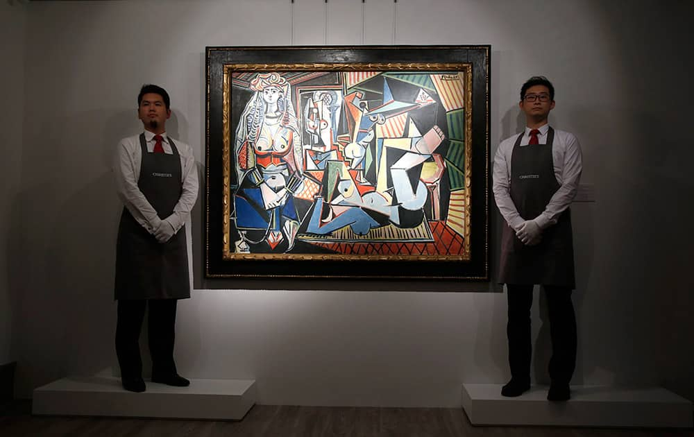 Staff members from Christie's auction house stand next to the painting 'Les Femmes d'Alger (Version 