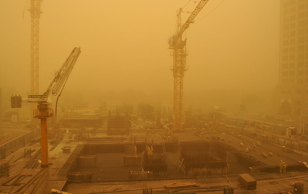 Migrant laborers, some wearing face masks, work on a construction site during a sandstorm in Dubai, United Arab Emirates.