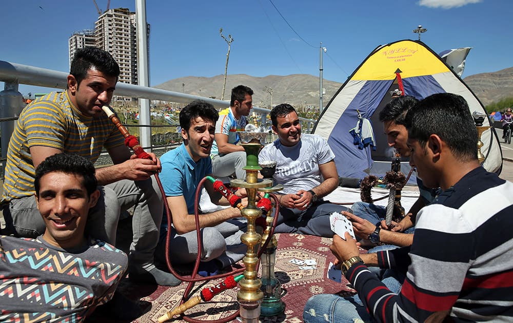 Two Iranian men smoke a water pipe as others play cards while spending their time outdoors observing the ancient festival of Sizdeh Bedar, an annual public picnic day on the 13th day of the Iranian new year, a legacy from pre-Islamic era, in the last day of Persian New Year holiday at the Pardisan Park in Tehran, Iran.