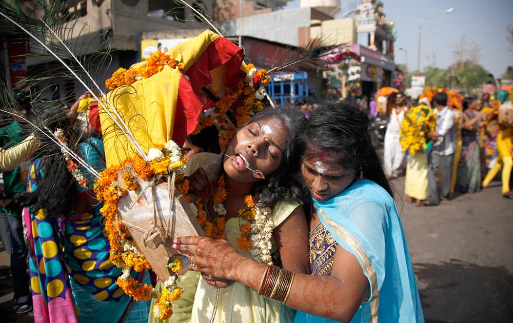 A woman tries to control a devotee in trance with her tongue pierced with a metal rod, on her way to a temple of Lord Murugan, on the occasion of Panguni Uthiram festival, in Ahmedabad.