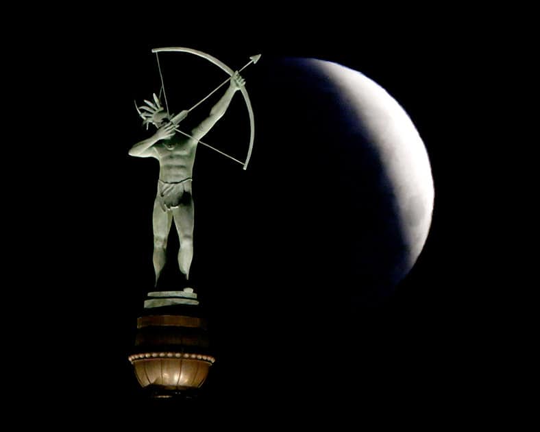 A partially eclipsed full moon sets behind a statue of a Kansa Indian at the Kansas Statehouse.