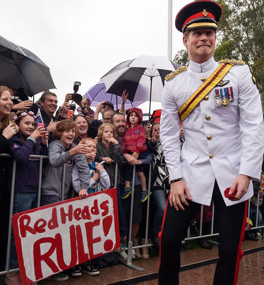 Britain's Prince Harry reacts after shaking hands with kids holding up a sign reading 