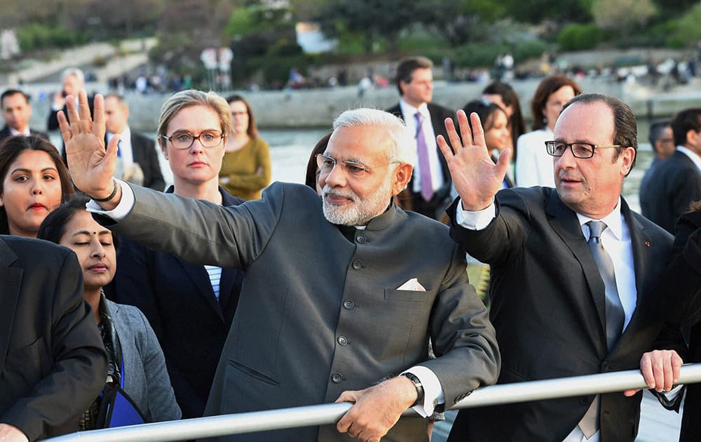 Prime Minister Narendra Modi with French President Francois Hollande wave during a boat ride on the Seine River, past the Eiffel Tower, in Paris.