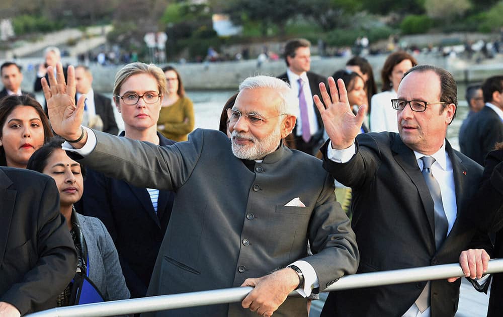 Prime Minister Narendra Modi with French President Francois Hollande wave during a boat ride on the Seine River, past the Eiffel Tower, in Paris