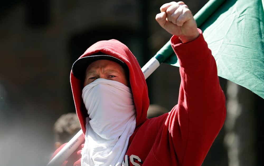 A masked protester raises a clenched fist while listening to a speaker at a rally for fair wages in Seattle.