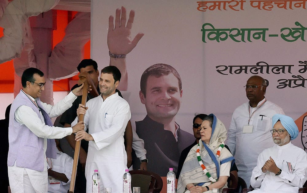 Congress Vice President being handed over a large wooden plough by party leader Ajay Maken as Sonia Gandhi and Former Prime Minister Manmohan Singh look on during the farmers rally at Ramlila Maidan in New Delhi.