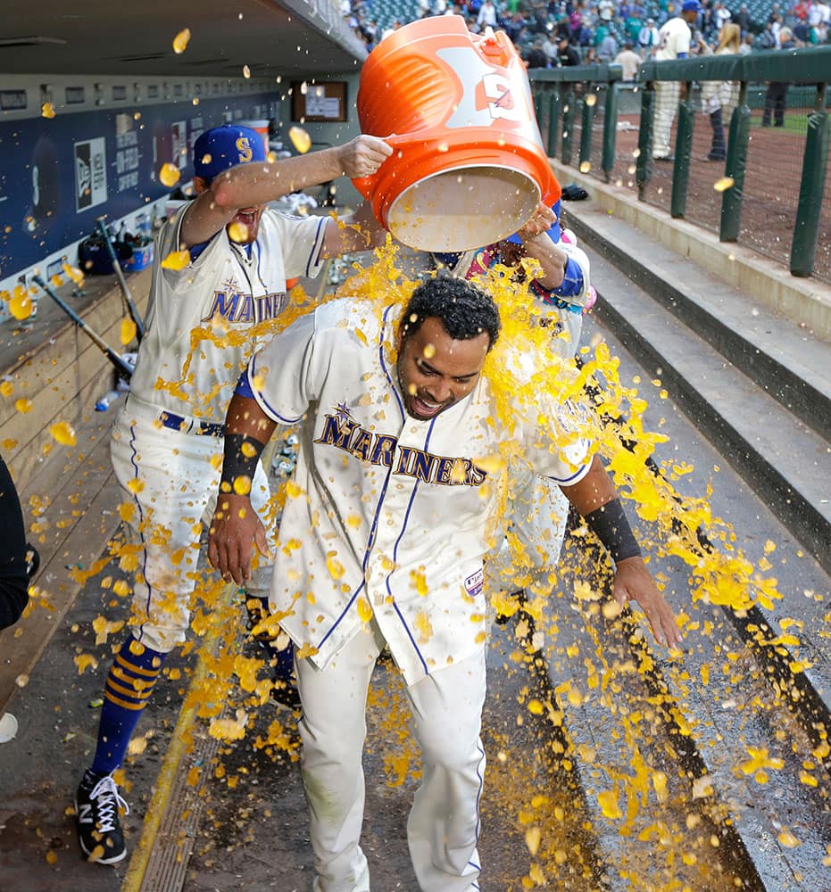Seattle Mariners' Nelson Cruz, foreground, is doused by Mariners pitchers Charlie Furbush, left, and Danny Farquhar, right, as he takes part in a television interview after hitting a walkoff RBI-single in the ninth inning of a baseball game against the Texas Rangers, in Seattle. 