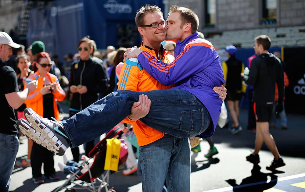 Tim Meyers of Strongsville, Ohio, plants a kiss on the cheek of his brother Jeff Meyers, of Sagamore Hills, Ohio, while posing for photos with friends at the finish line of the 119th Boston Marathon in Boston, Mass.