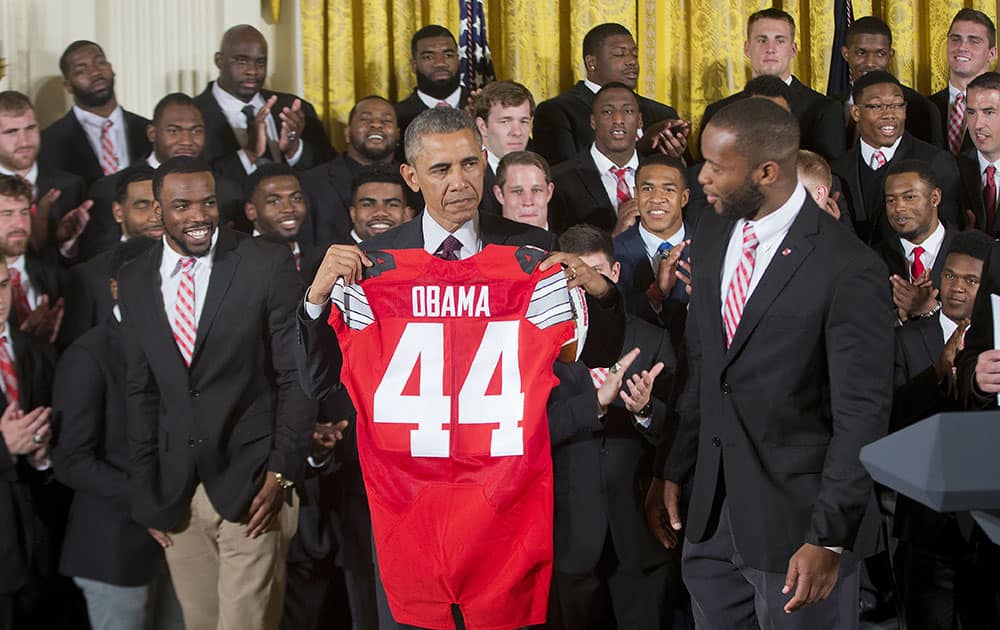 President Barack Obama holds a Ohio State football jersey presented, by Ohio State football players players Curtis Grant, right, and Doran Grant, left, as he welcomed the NCAA College Football Playoff National Champion Ohio State Buckeyes, during a ceremony in the East Room of the White House in Washington.