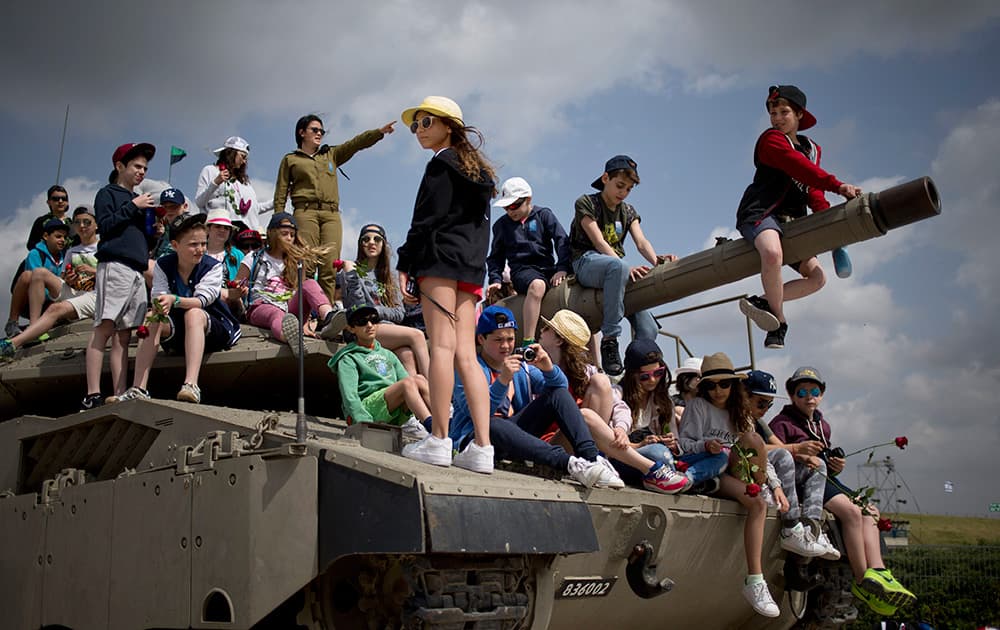 School children from Belgium sit on a tank on display as they listen to an Israeli soldier speaks about Israel's wars, near the wall of names of fallen soldiers, at the Armored Corps memorial, before a ceremony marking the annual Memorial Day for soldiers and civilians killed in more than a century of conflict between Jews and Arabs, in Latrun near Jerusalem, Israel.