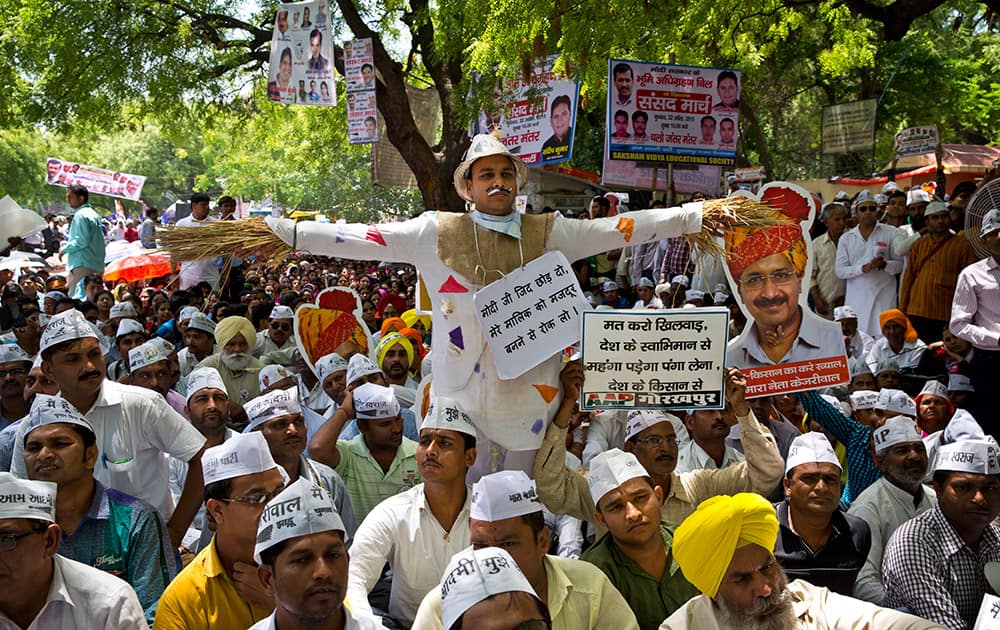 A man stands dressed like a scare crow as farmers and Aam Aadmi Party supporters display pictures of Delhi Chief Minister leader Arvind Kejriwal at a rally near the parliament in New Delhi.