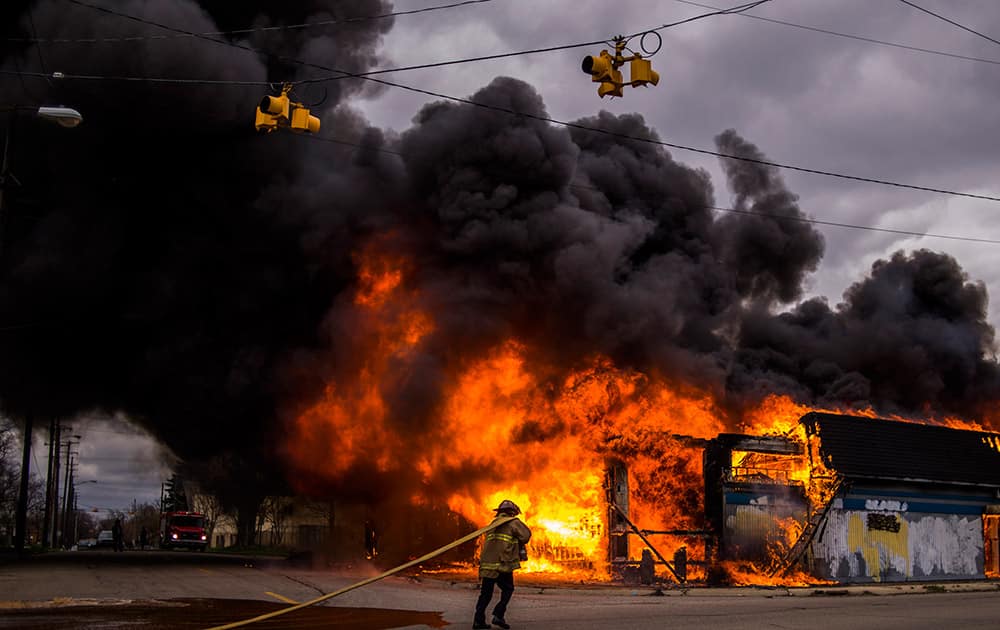 Flint firefighters work to contain a large fire that engulfs a former strip club, once called The Body Shop at the intersection of Glenwood Avenue and Asylum Street, sending a large plume of black smoke over the city of Flint, Mich. 