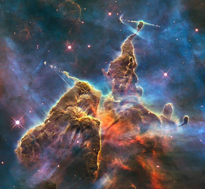 This image made by the NASA/ESA Hubble Space Telescope shows a three-light-year-tall pillar of gas and dust in the Carina Nebula which is being eaten away by the light from nearby bright stars. Inside, infant stars fire off jets of gas that can be seen streaming from towering peaks.