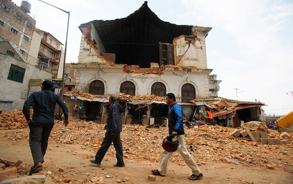 People walk past a building that was damaged in an earthquake in Kathmandu, Nepal. A strong magnitude-7.9 earthquake shook Nepal's capital and the densely populated Kathmandu Valley before noon Saturday, causing extensive damage with toppled walls and collapsed buildings, officials said.