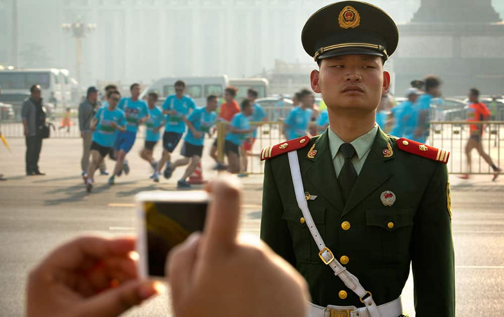 A spectator takes a photo of runners in a 10-kilometer (6.25 mile) road race as a Chinese paramilitary policeman stands guard near Tiananmen Square in Beijing.