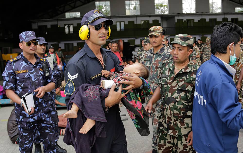 An Indian Air Force person carries a Nepalese child, wounded in Saturday’s earthquake, to a waiting ambulance after the child and mother were evacuated from a remote area at the airport in Kathmandu, Nepal.