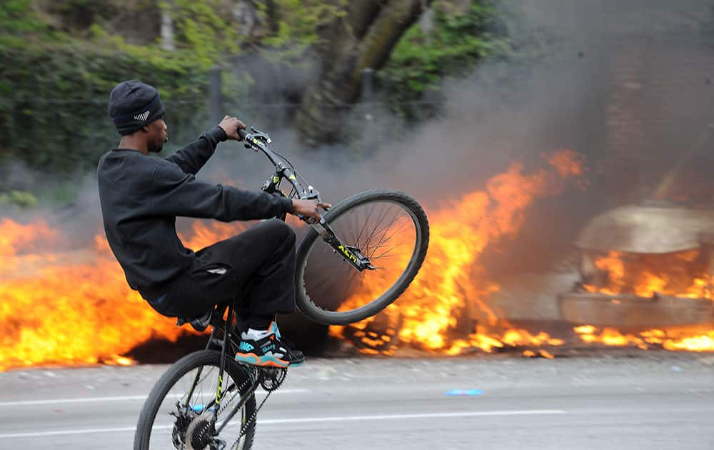 A cyclist rides by burning police cars, during unrest following the funeral of Freddie Gray in Baltimore. Rioters plunged part of Baltimore, torching a pharmacy, setting police cars ablaze and throwing bricks at officers.